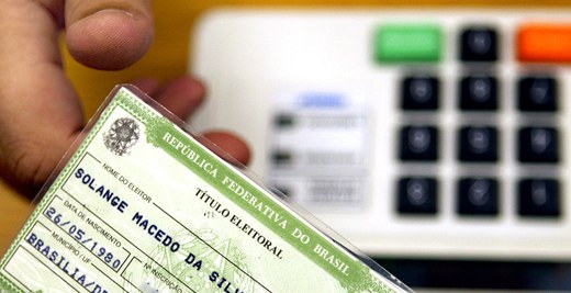 Título eleitoral Homem segurando título eleitoral e leitor biométrico ao fundo.